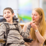 This is an image of a male student in a wheelchair and their female teacher is next to them. 